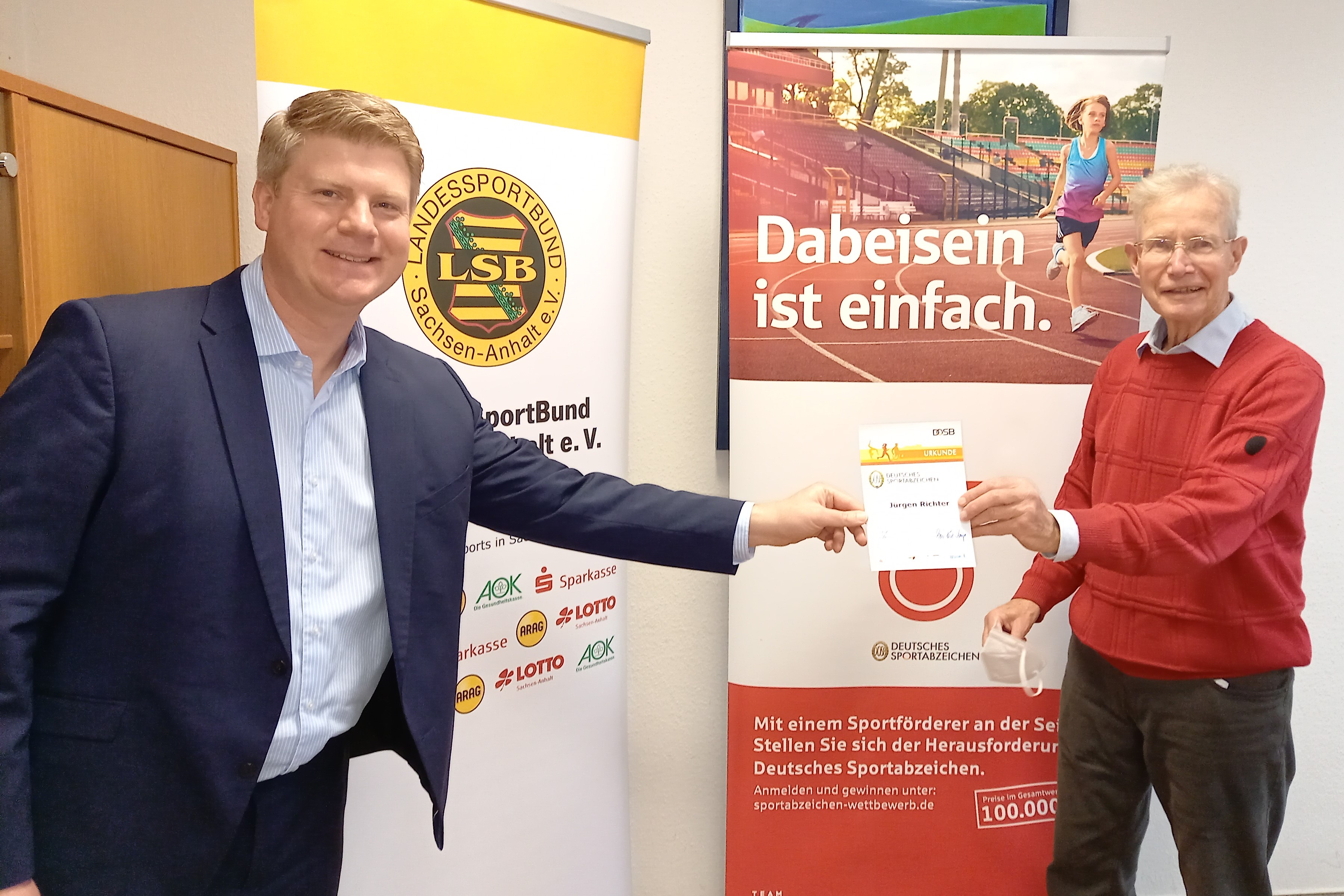 LSB-Vorstandsvorsitzender Tobias Knoch gratuliert Jürgen Richter zum 60. Deutschen Sportabzeichen.